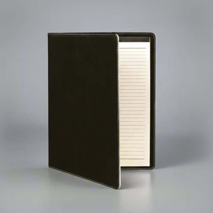 A black leather-bound notebook stands open on a gray surface, revealing lined pages inside.